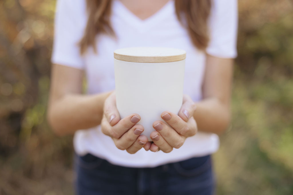 Two hands offering a Joy Candle Co. candle outdoors in golden autumn light