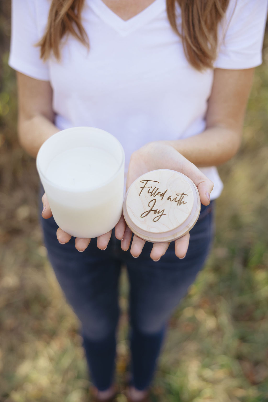 Hands holding a Joy Candle Co. candle and its wooden lid engraved with the words Filled with Joy
